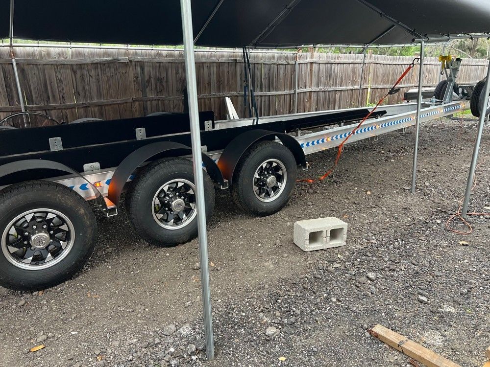 A boat trailer is parked under a tent in a gravel lot.