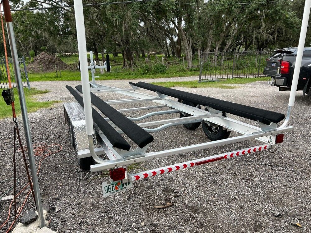 A boat trailer is parked in a gravel lot next to a truck.