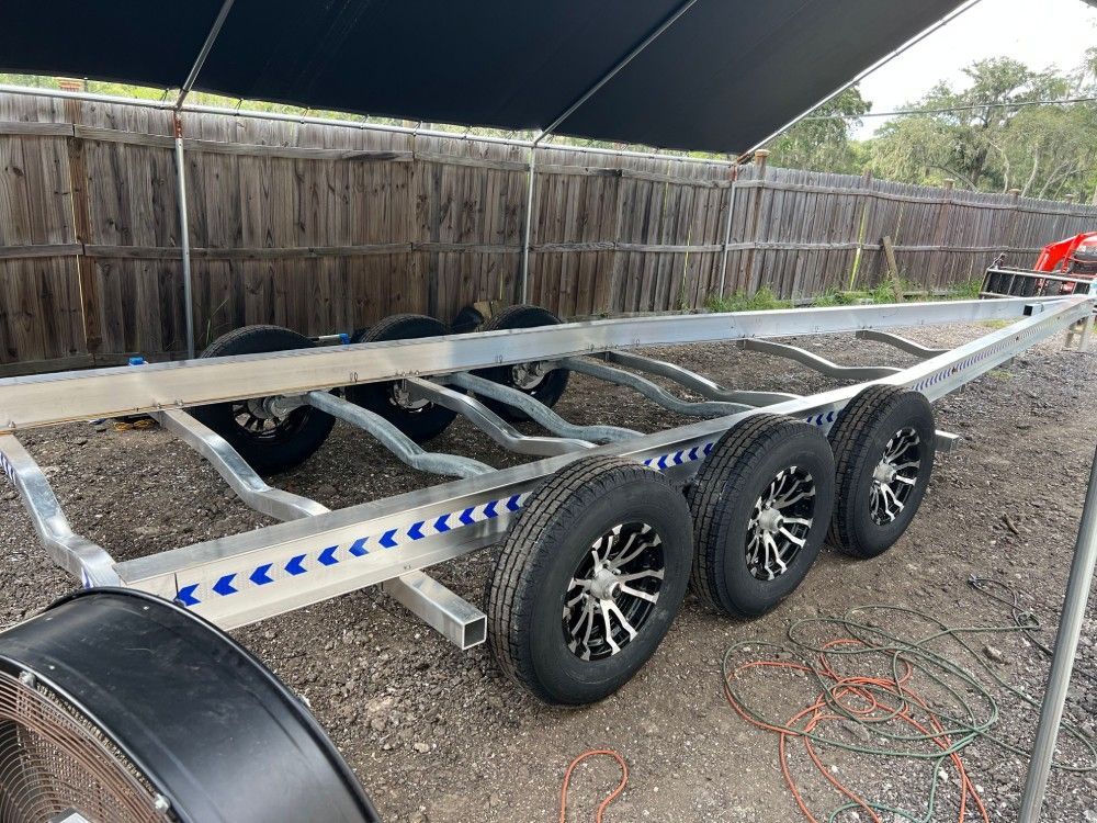 A boat trailer is parked in the dirt in front of a wooden fence.