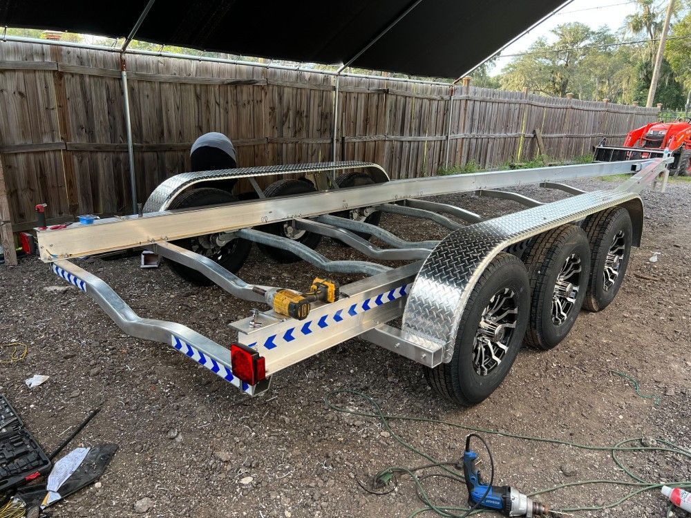 A boat trailer is sitting in a gravel lot next to a wooden fence.