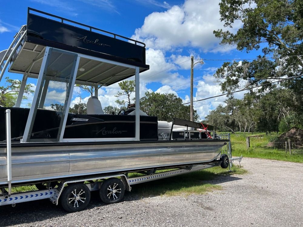 A pontoon boat is parked on a trailer in a parking lot.
