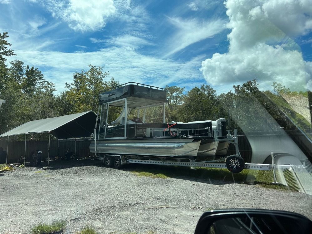 A pontoon boat is on a trailer in a parking lot.