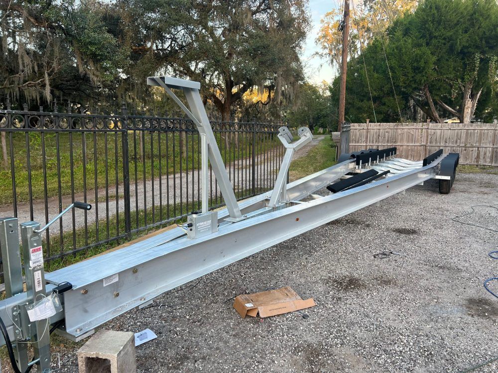 A boat trailer is sitting on the ground in front of a fence.