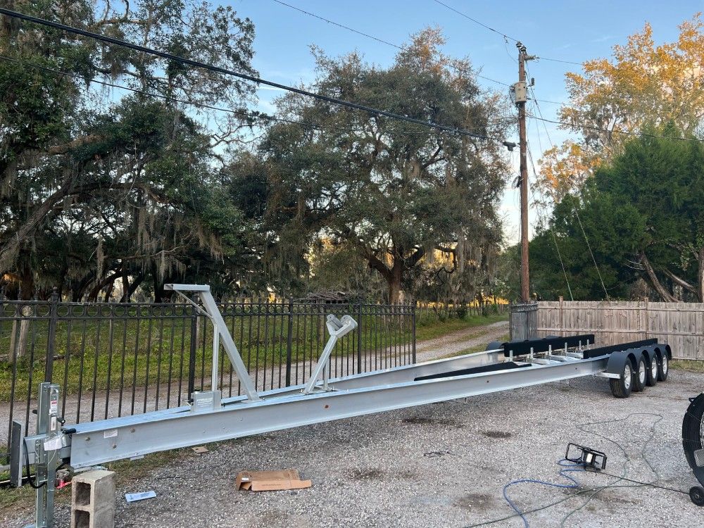 A boat trailer is sitting in a gravel lot next to a fence.