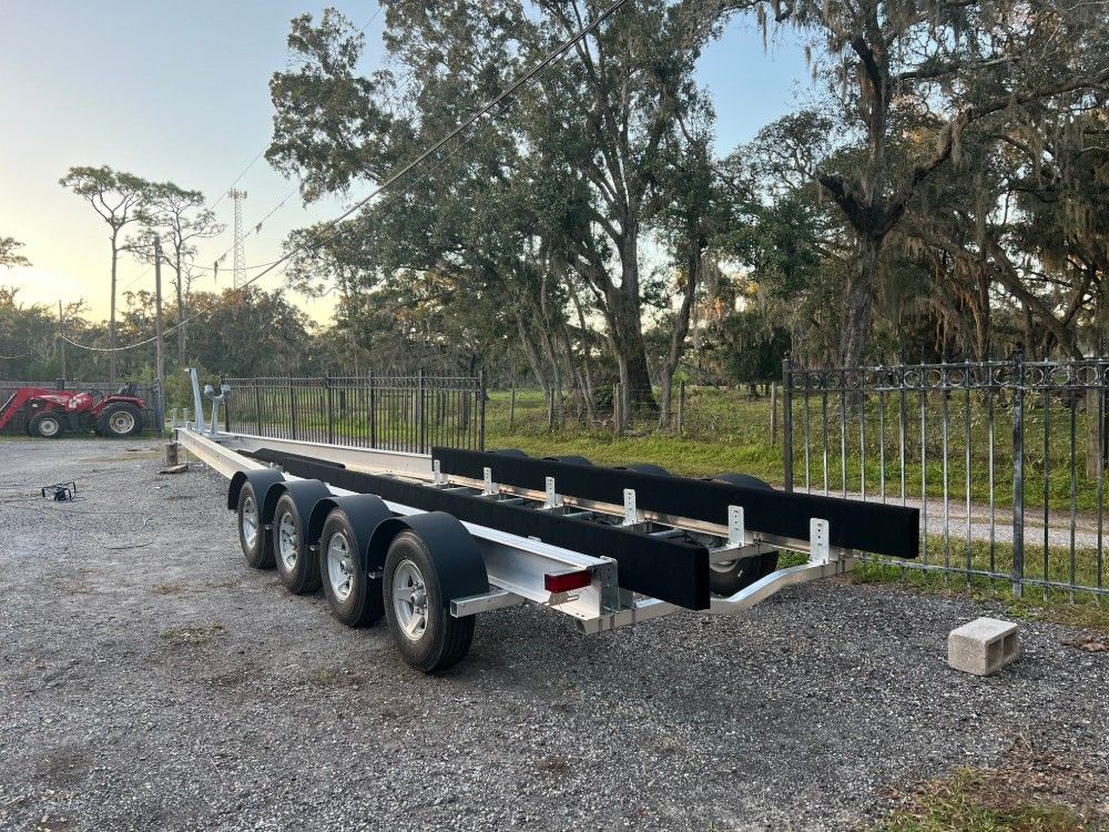 A boat trailer is parked in a gravel lot next to a fence.