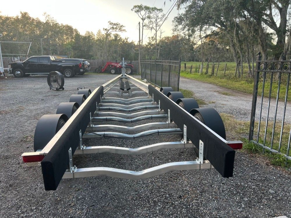 A boat trailer is parked in a gravel lot next to a fence.
