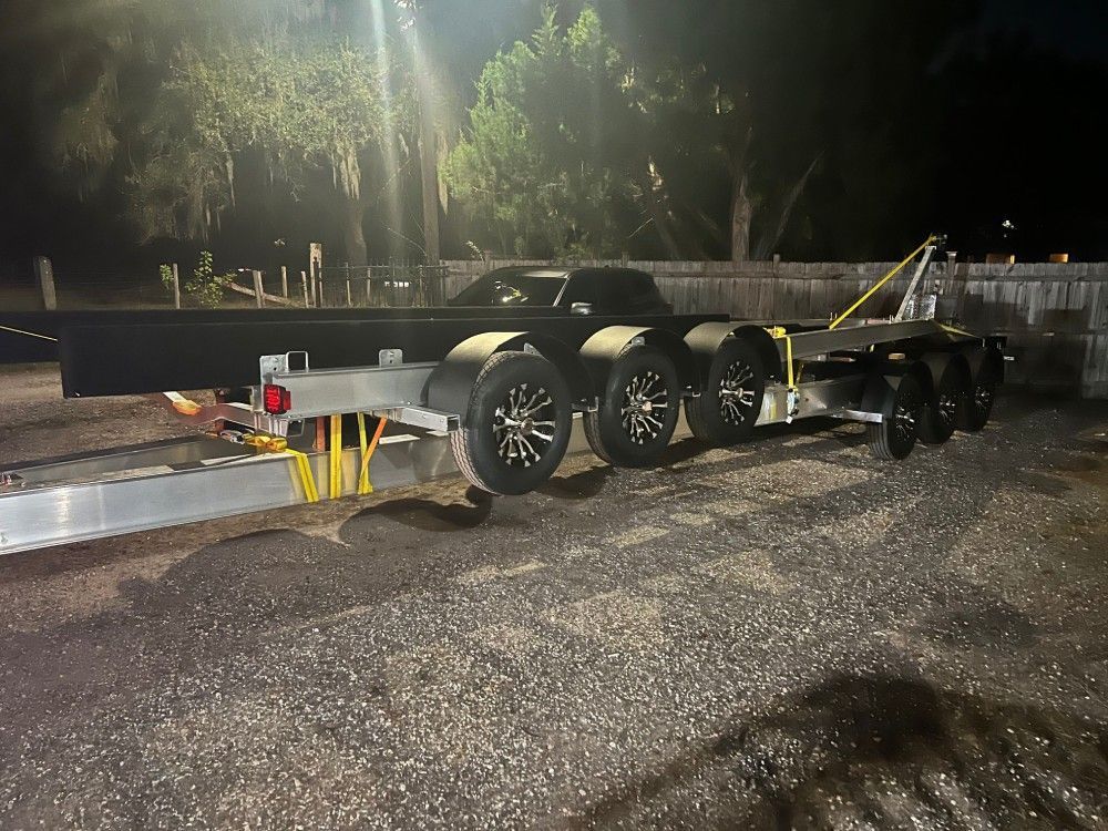 A trailer with a car on it is parked in a parking lot at night.