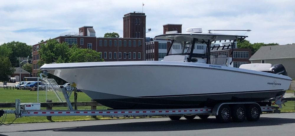 A white boat is on a trailer with a building in the background.
