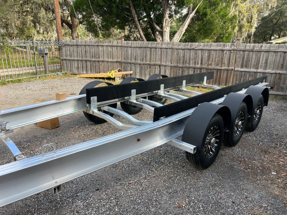 A boat trailer is parked in front of a wooden fence.