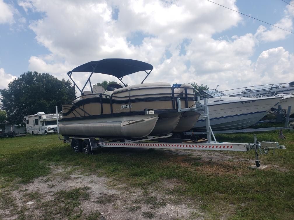 A pontoon boat is parked on a trailer in a grassy field.