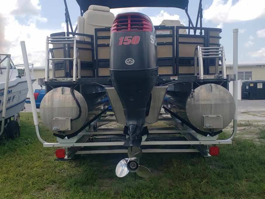 A pontoon boat with a mercury outboard motor is parked in the grass.