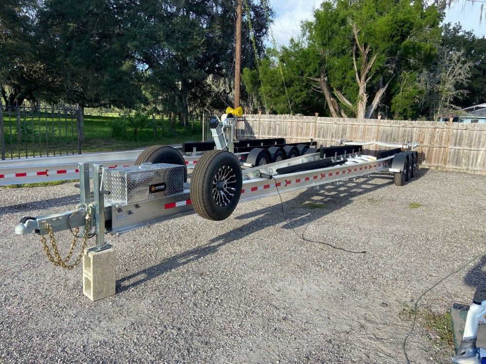 A boat trailer is parked in a gravel lot next to a fence.