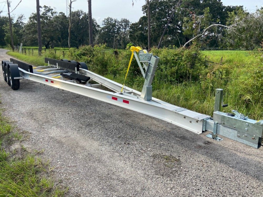 A boat trailer is parked on the side of a gravel road.