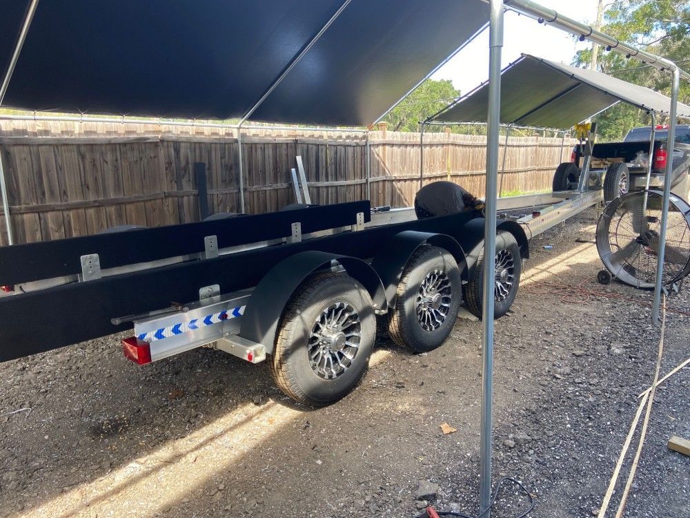 A boat trailer is parked under a tent in a gravel lot.
