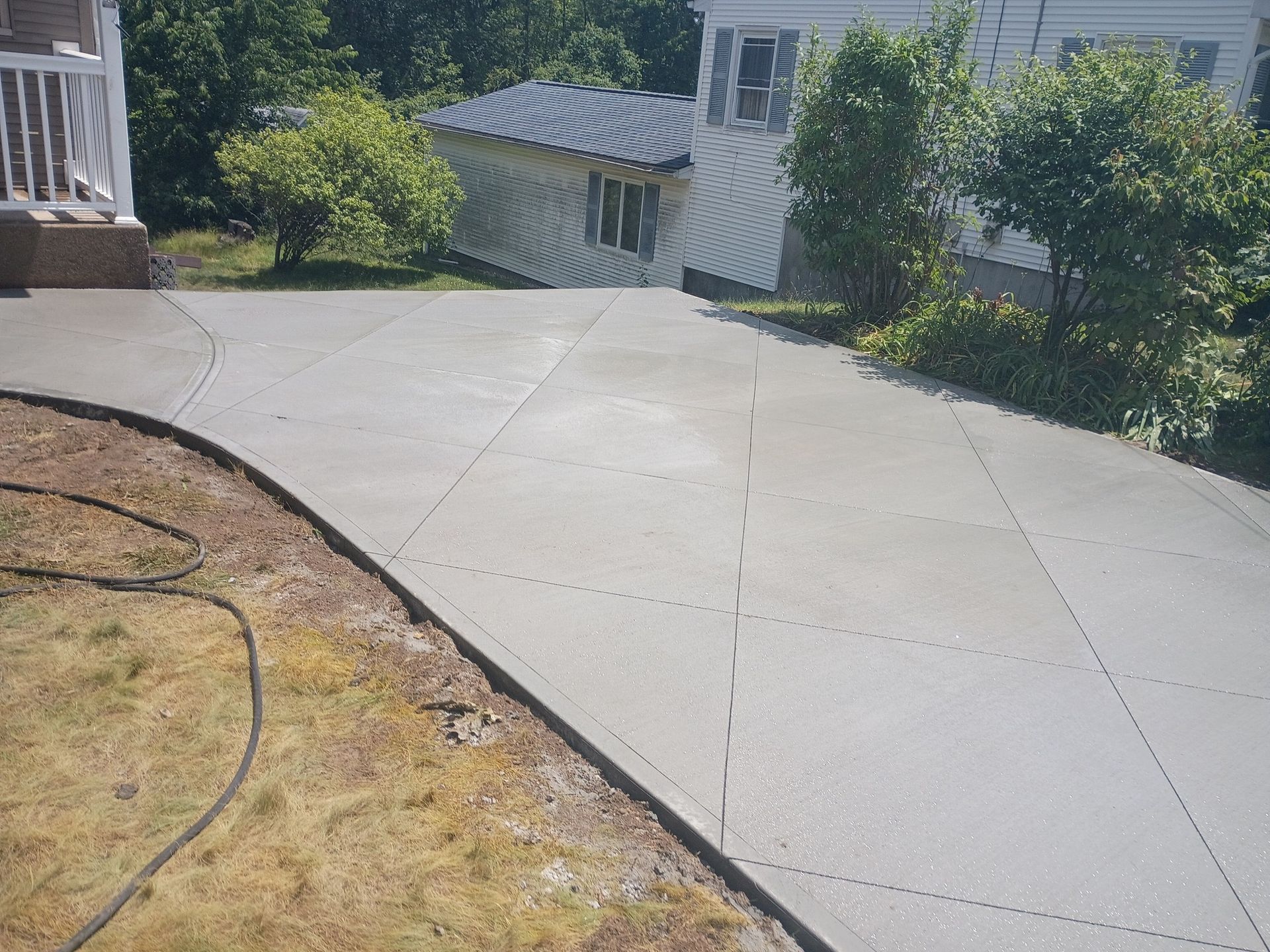 A newly poured gray concrete patio with a decorative diamond-patterned control joint design in a residential yard.