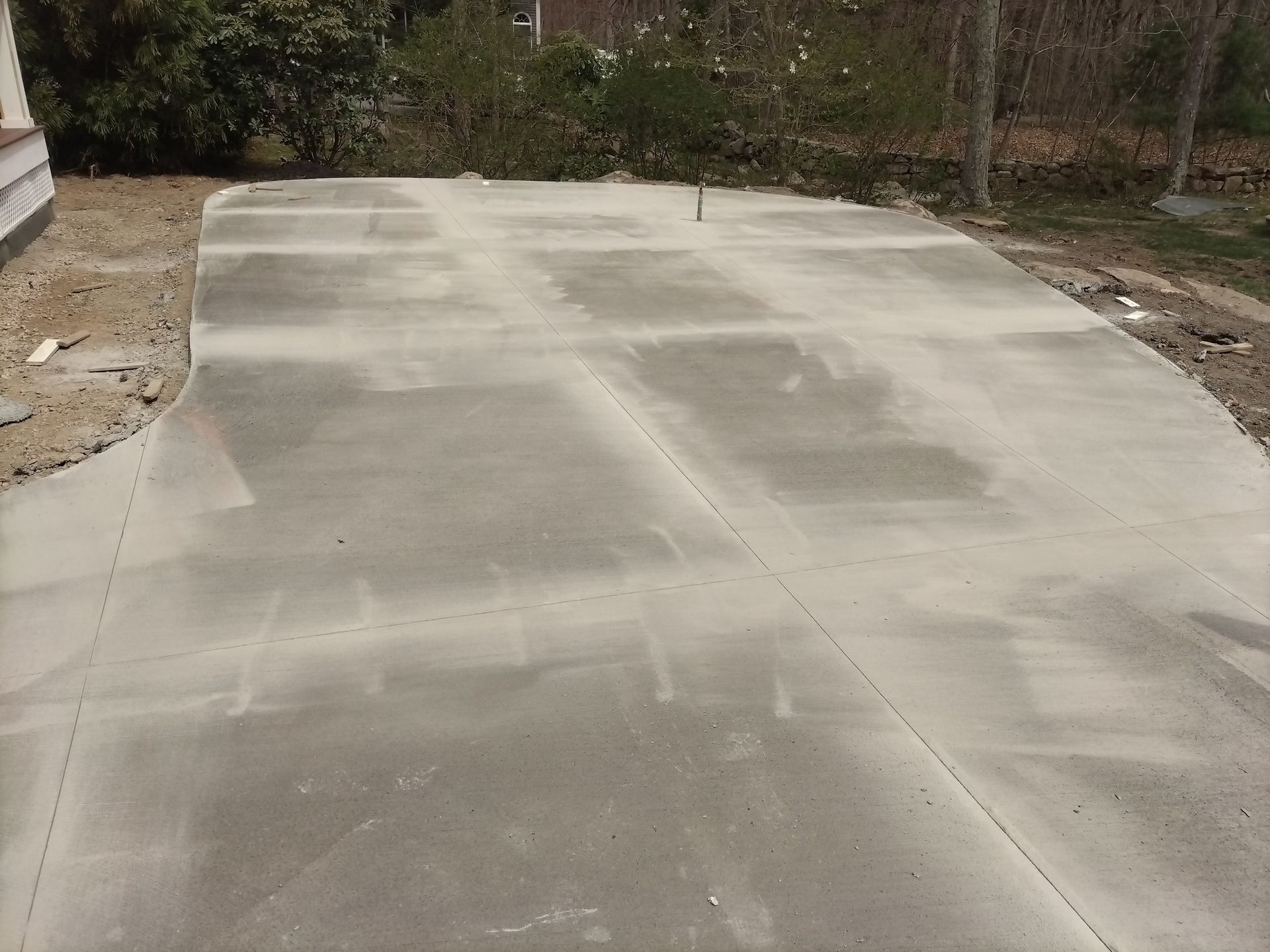 A freshly poured concrete driveway in a yard with a light gray surface and visible control joints.