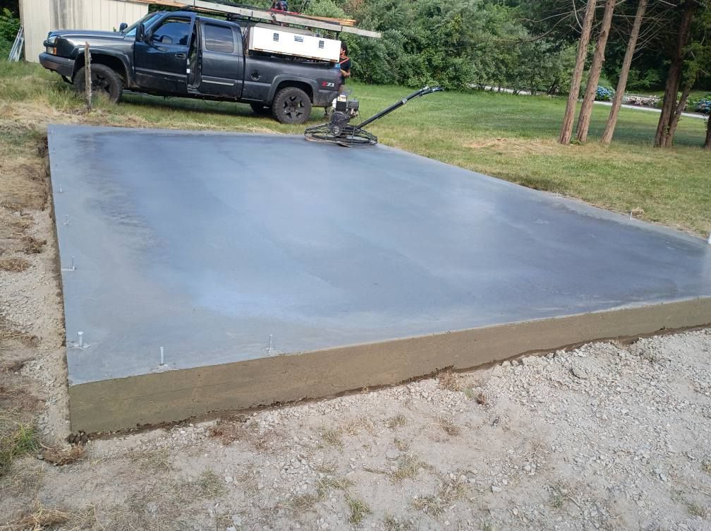 Freshly poured rectangular concrete slab in an outdoor setting with a dark pickup truck parked in the background.