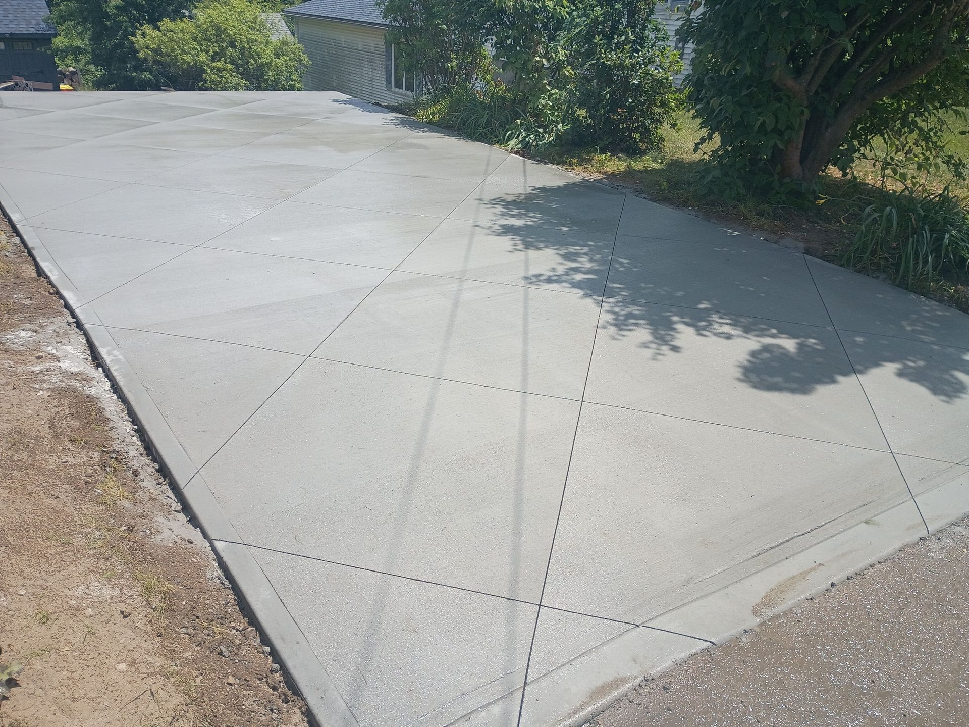 A newly poured concrete driveway features decorative diamond-shaped scores in an outdoor residential setting.