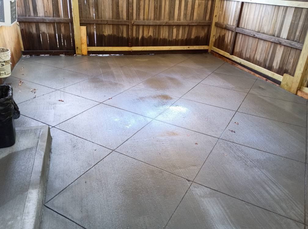 A freshly poured gray concrete patio with a diamond-patterned groove finish, located next to a wooden fence.