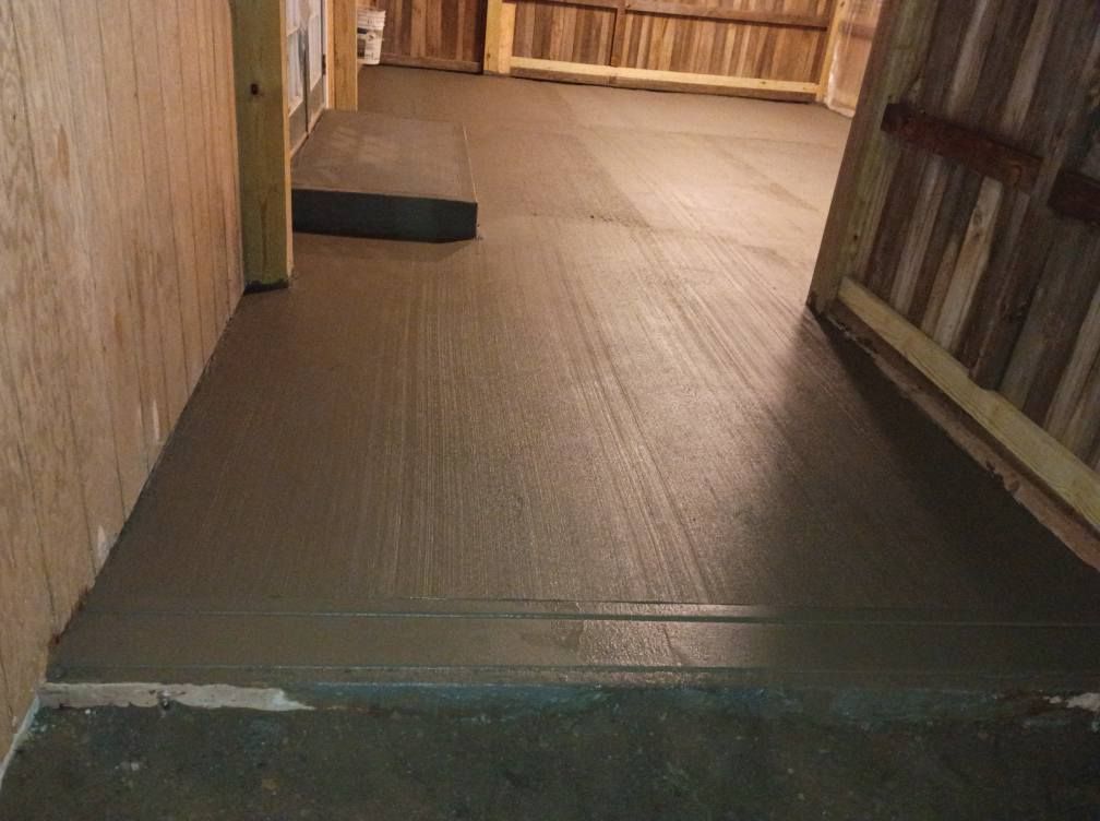 Freshly poured gray concrete floor in a workshop, featuring a smooth transition ramp and wood-paneled walls.