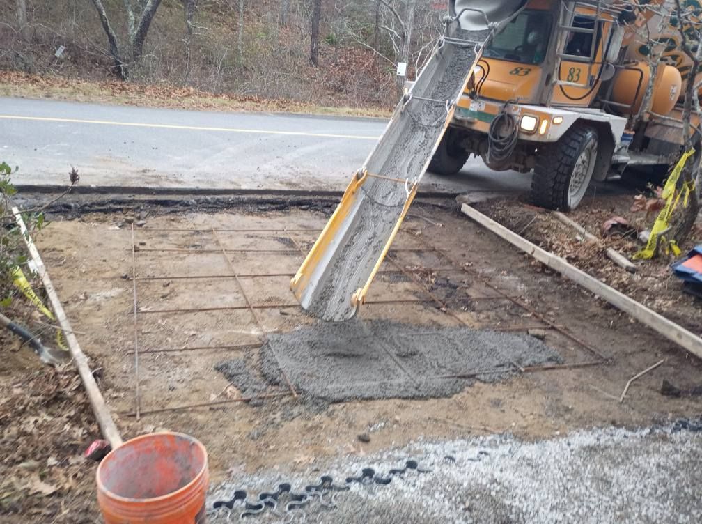 A concrete truck pours wet cement onto wire mesh within wooden forms on a dirt ground outdoors.