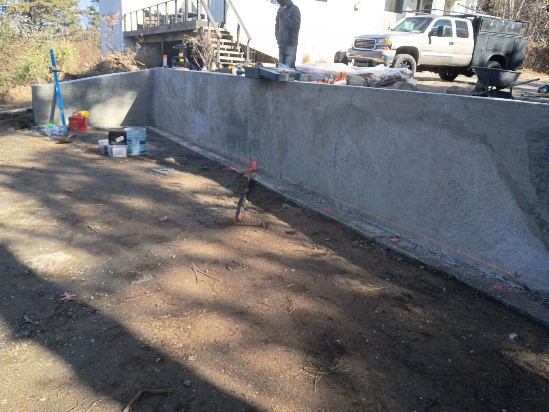 A freshly poured concrete retaining wall at a residential construction site, with a truck parked in the background.