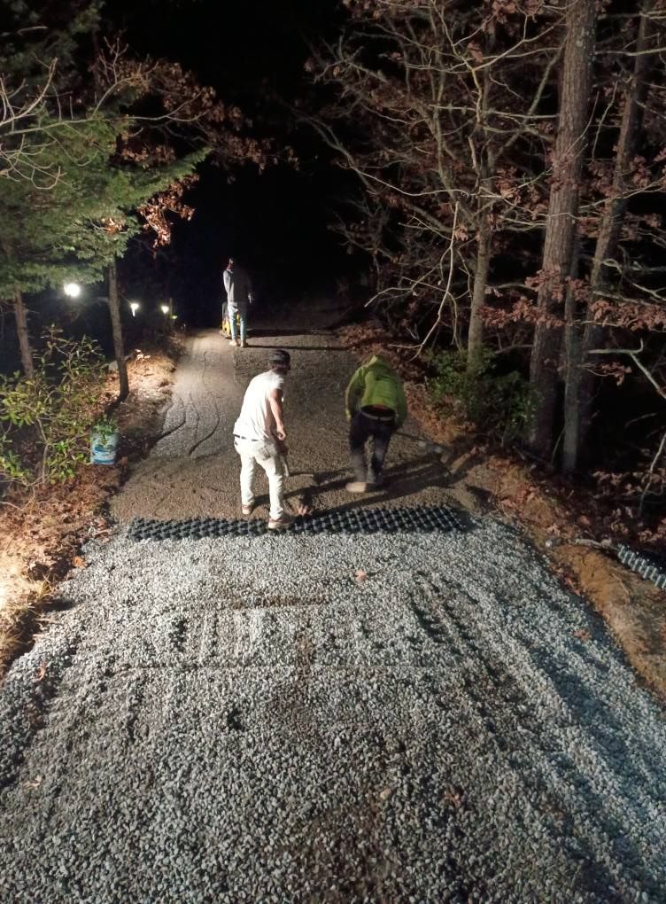Three people work on a gravel path at night, installing a black plastic grid system to stabilize the slope.
