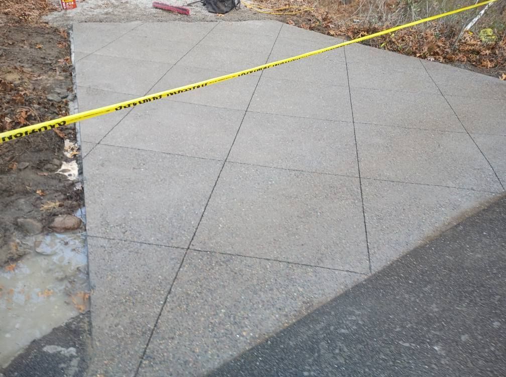 A newly poured concrete walkway with diamond-patterned grooves, partitioned by yellow caution tape.