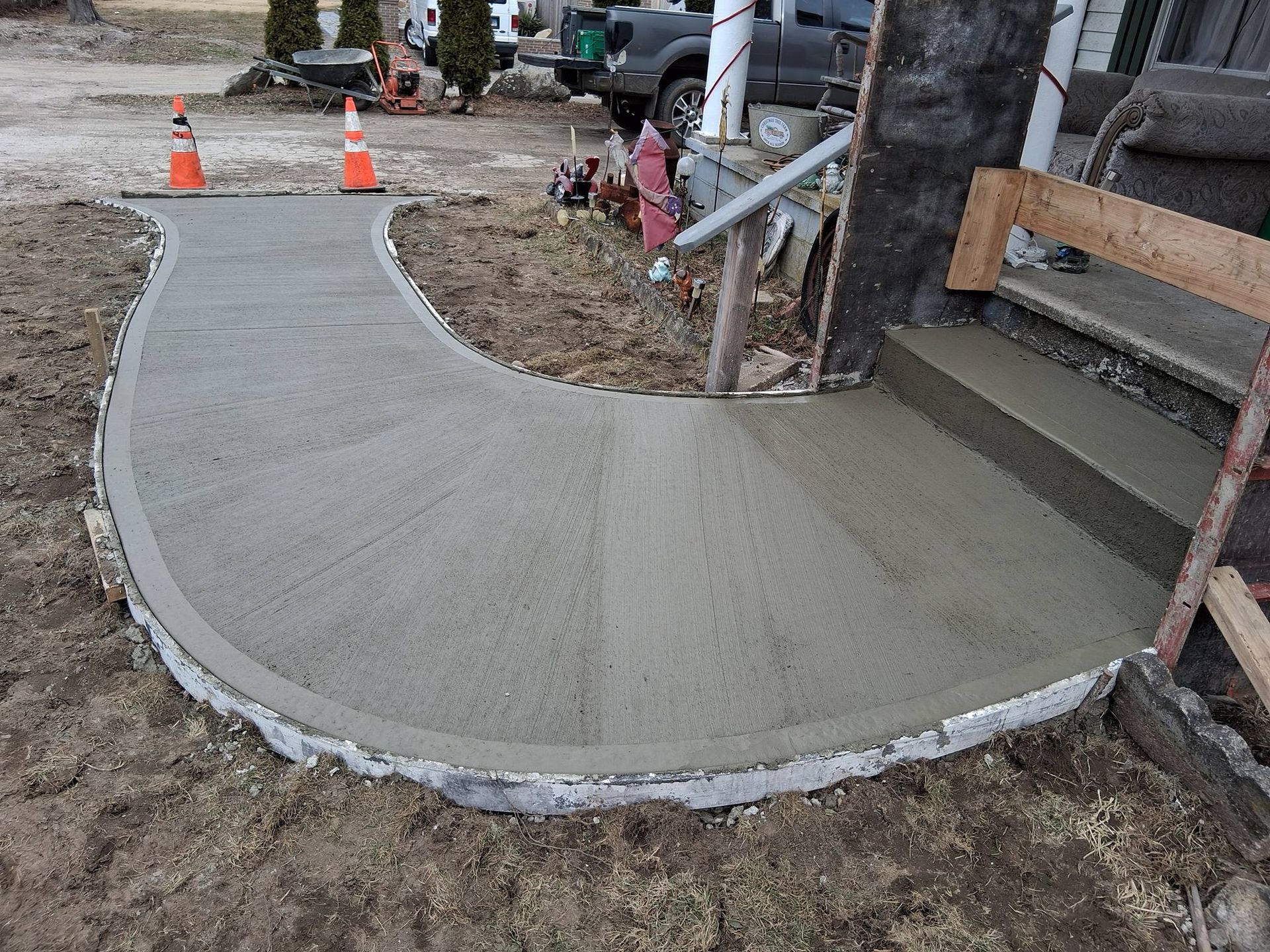 Freshly poured concrete walkway curving toward wooden porch steps at a construction site.