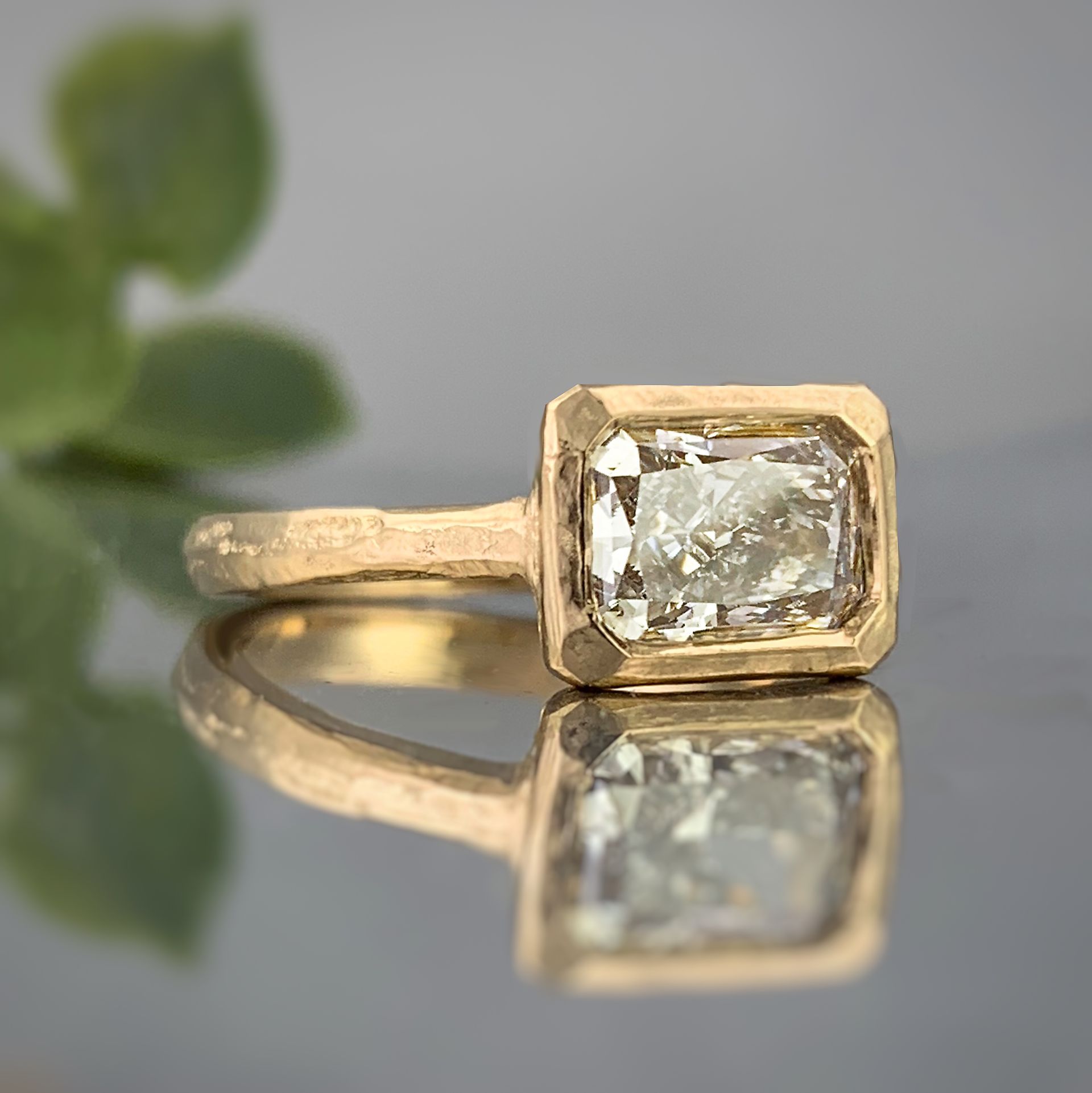 A gold ring with an emerald cut diamond is sitting on a table.