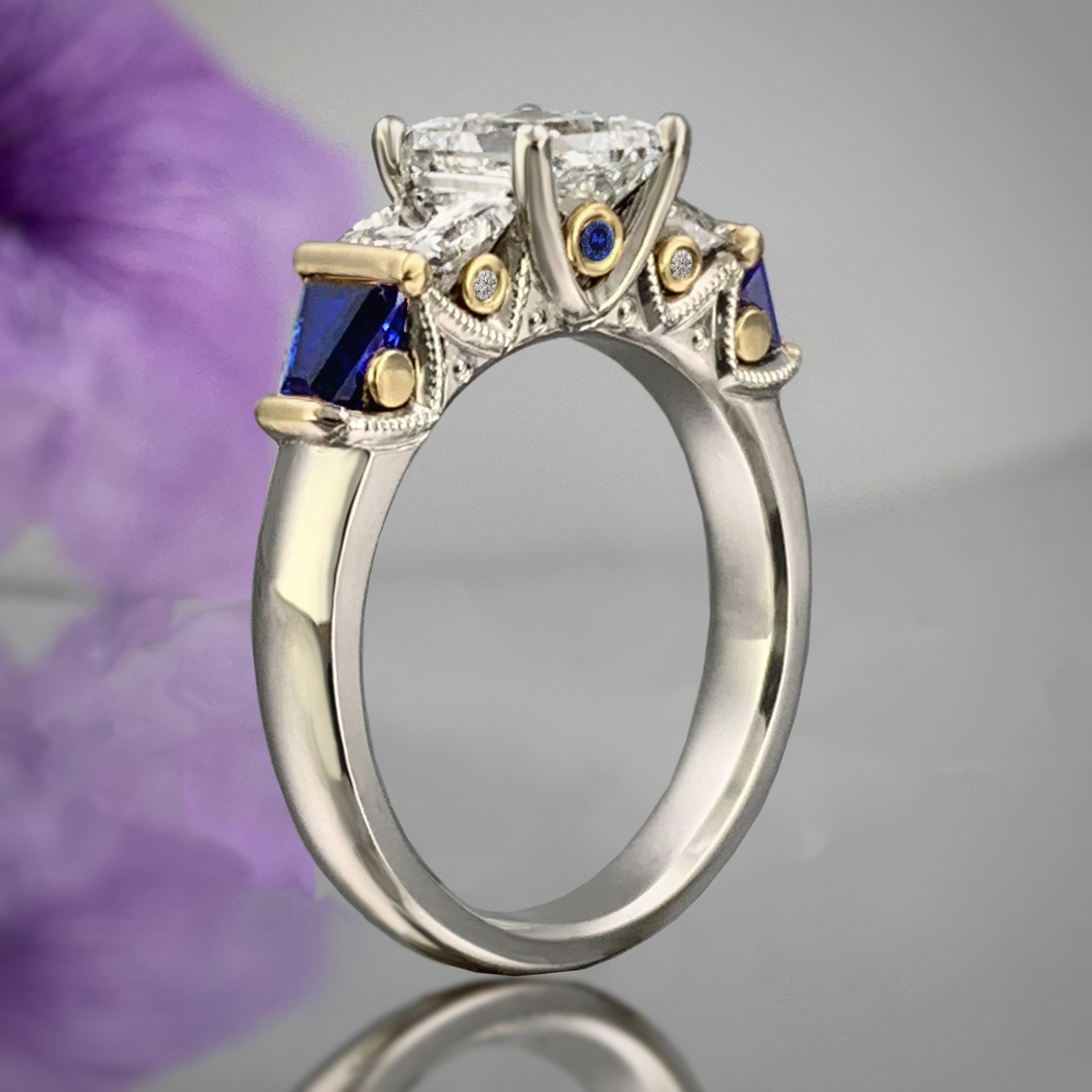 A diamond and sapphire ring with a purple flower in the background