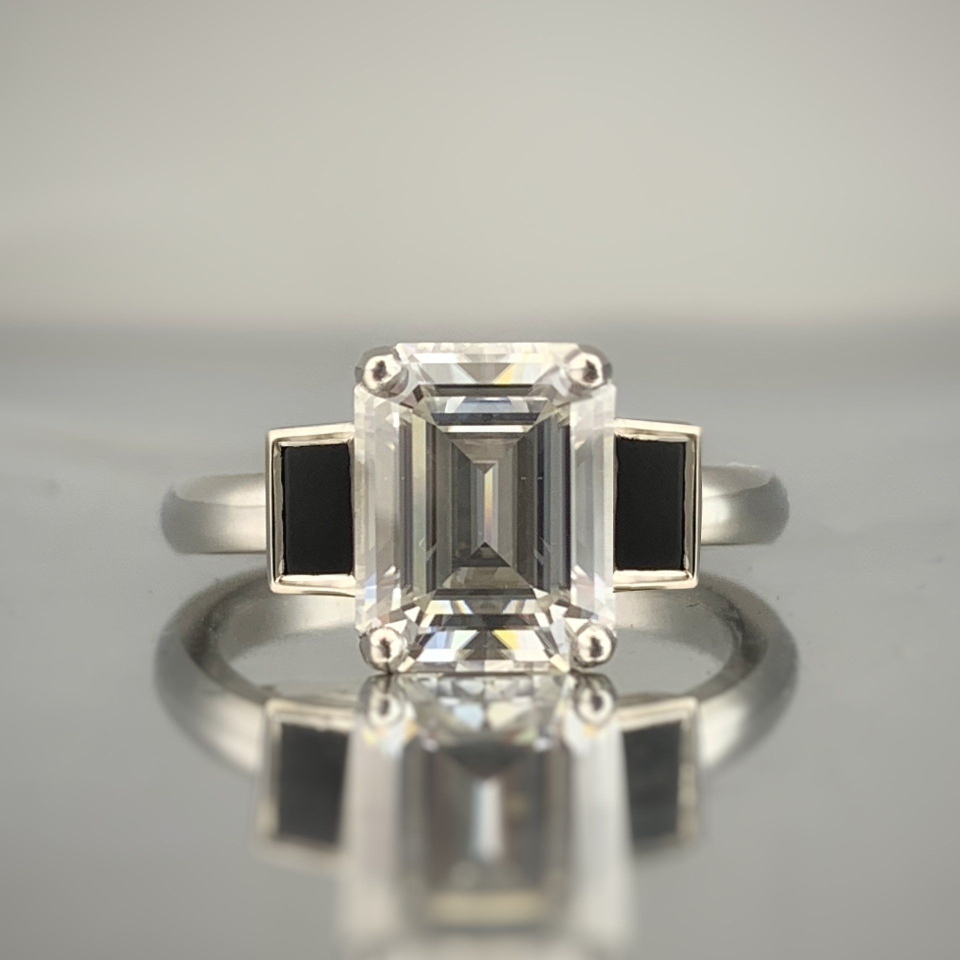 An emerald cut diamond ring is sitting on a table.