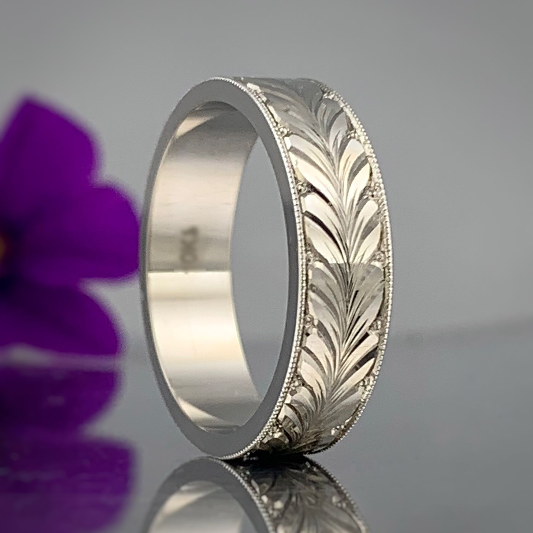 A silver ring is sitting on a table next to a purple flower