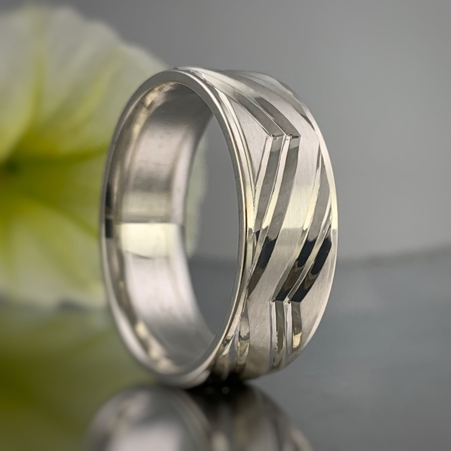 A silver ring is sitting on a table with a flower in the background