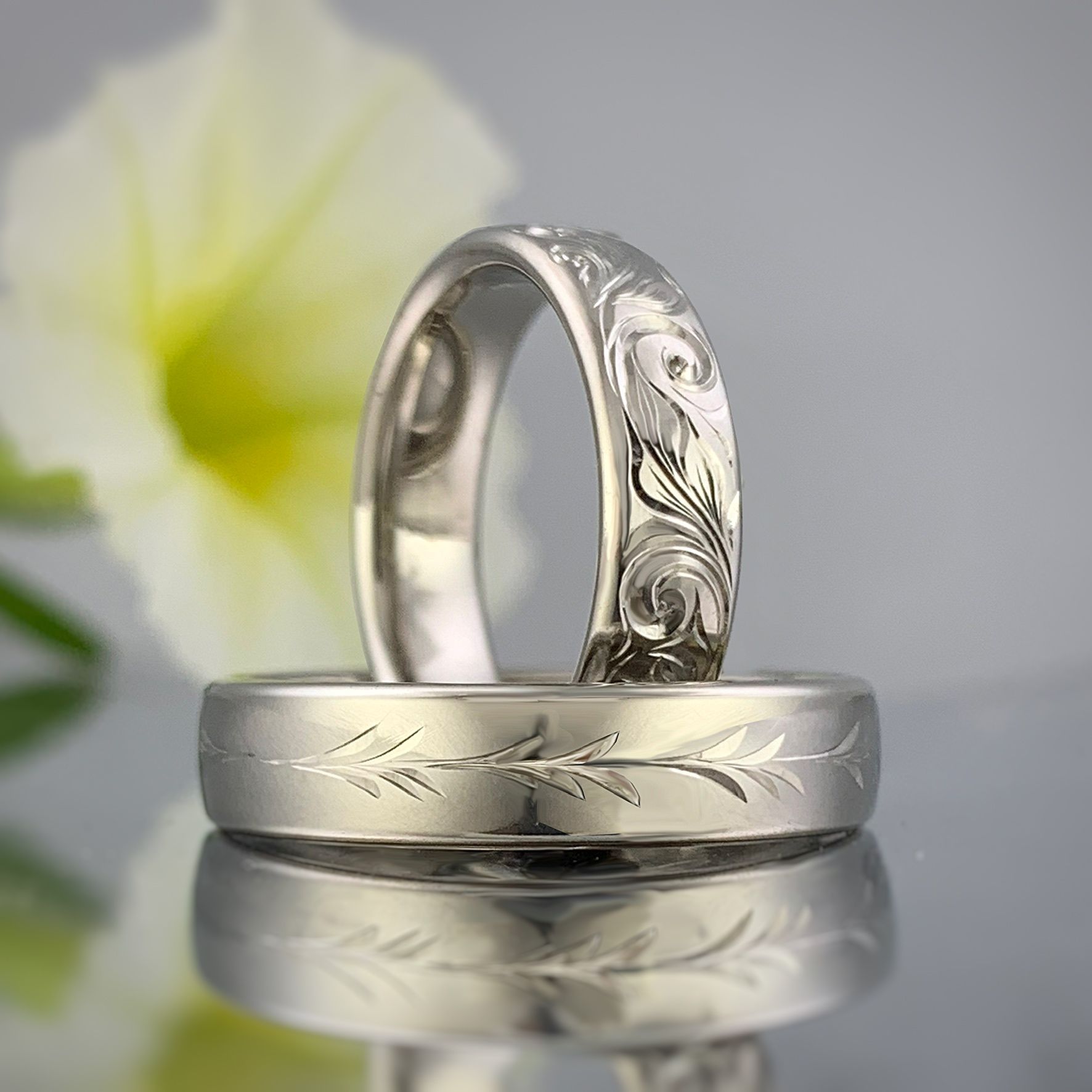 A pair of wedding rings are sitting on a table in front of a flower.