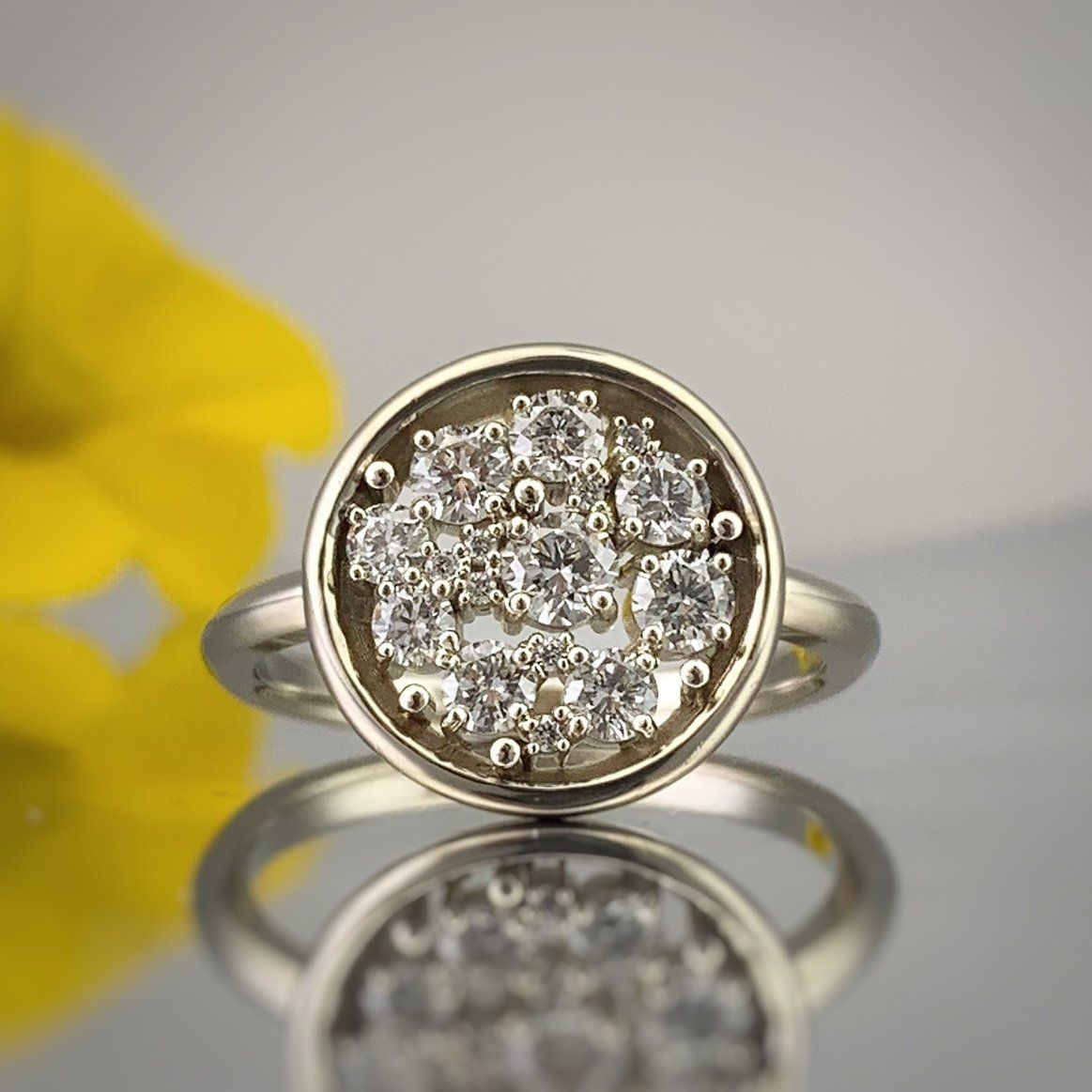 A ring with diamonds in it is sitting on a table next to a yellow flower.