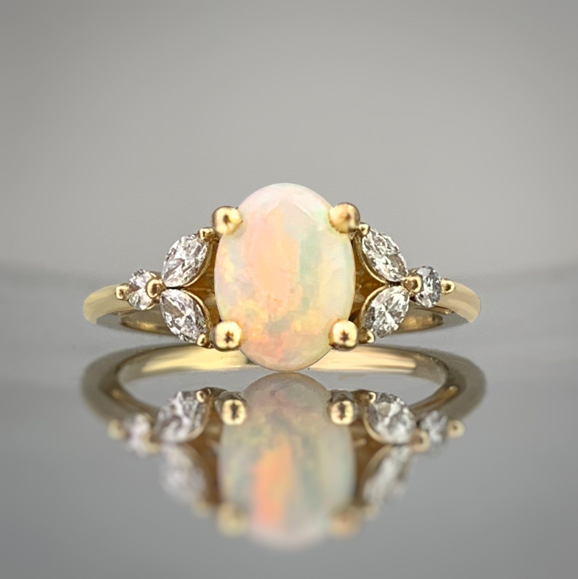 A yellow gold ring with an opal and diamonds on a table.