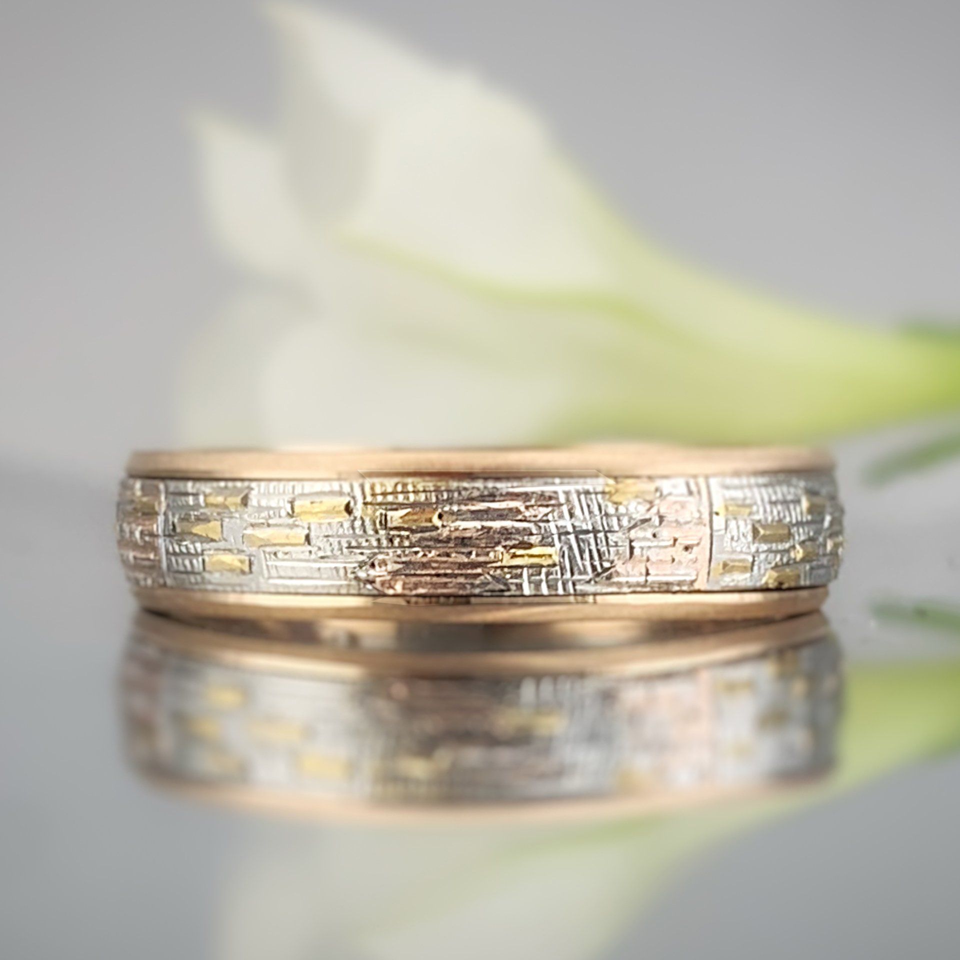 A close up of a wedding ring on a table with a flower in the background.