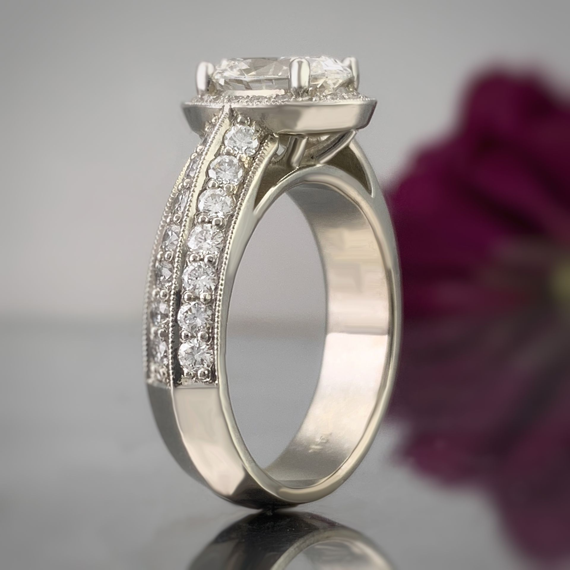 A diamond ring is sitting on a table in front of a purple flower