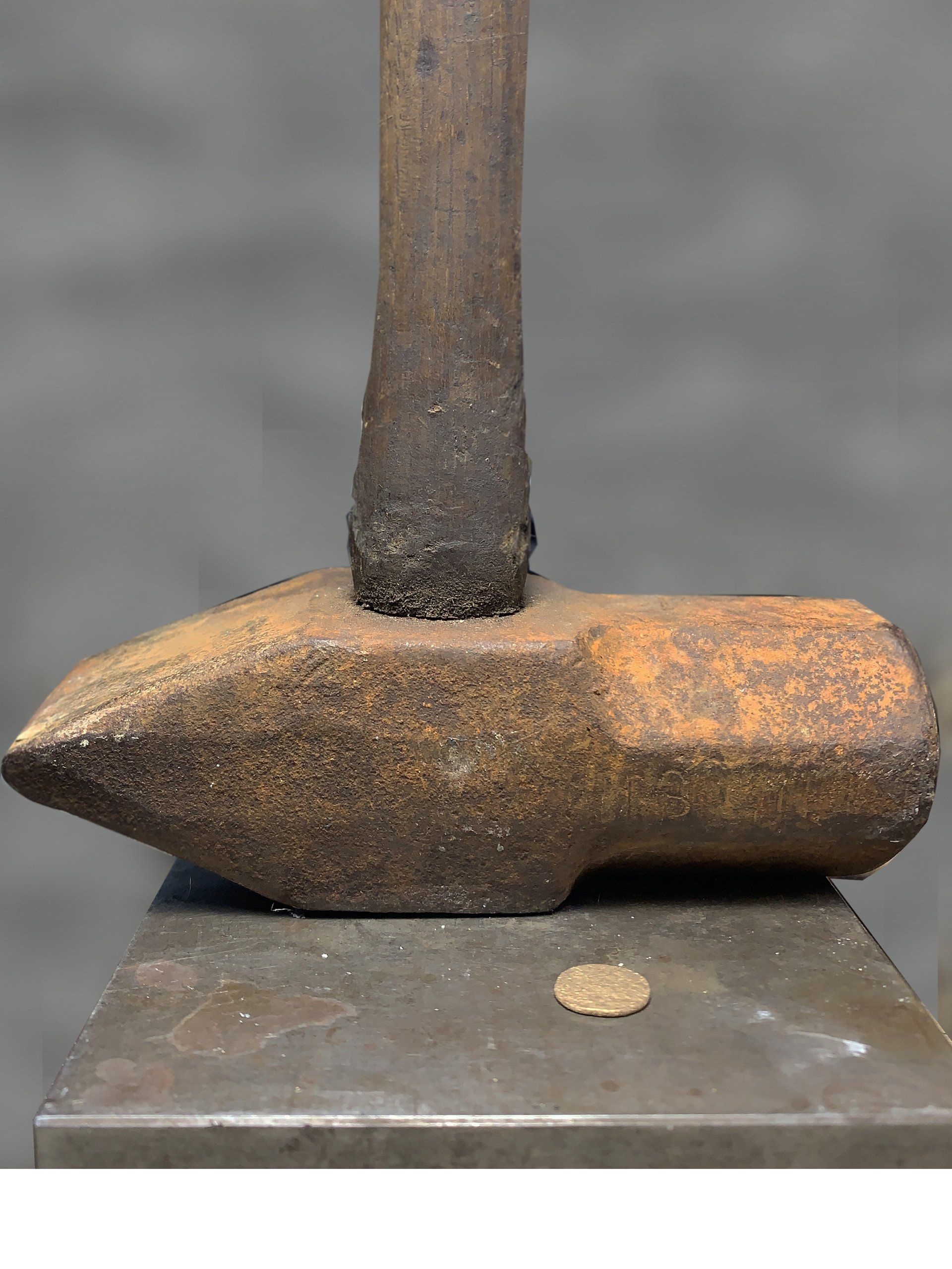 An old rusty hammer is sitting on top of an anvil next to a coin.