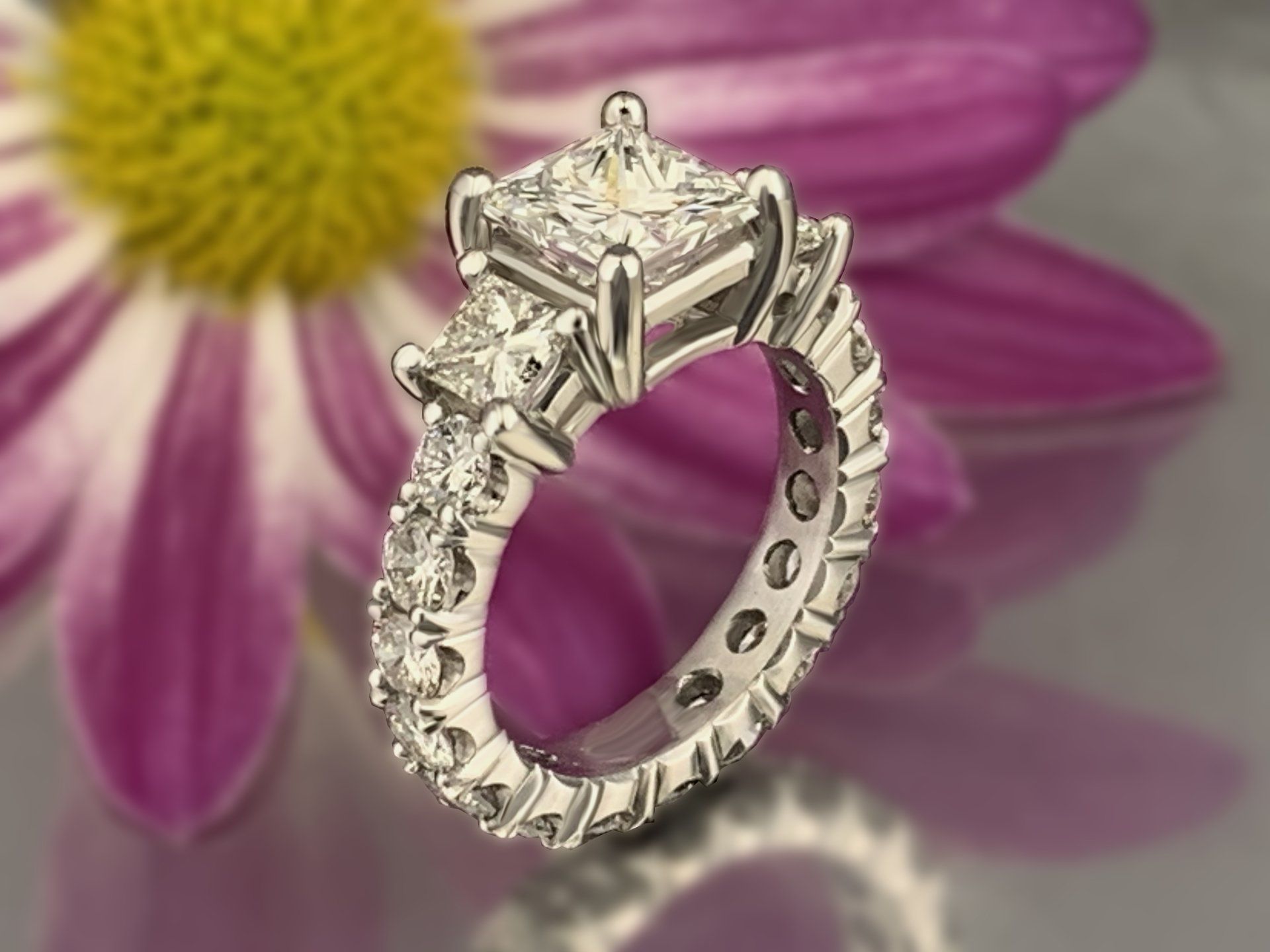 A diamond ring is sitting in front of a purple flower