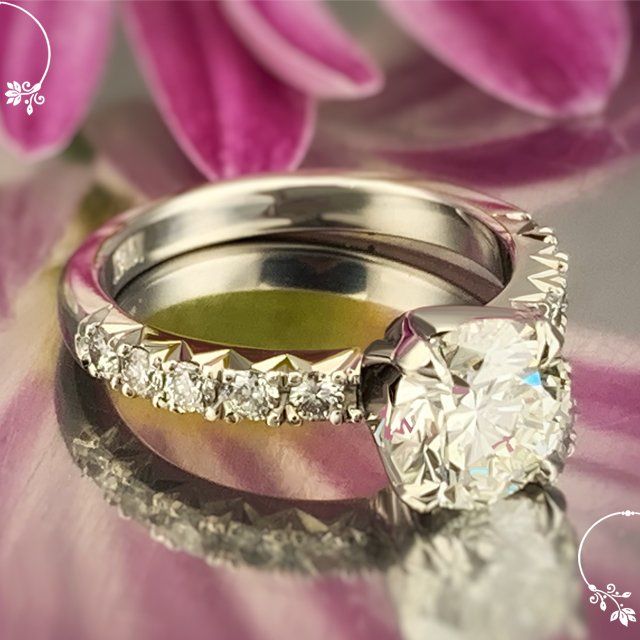 A wedding ring and engagement ring are sitting on a pink flower