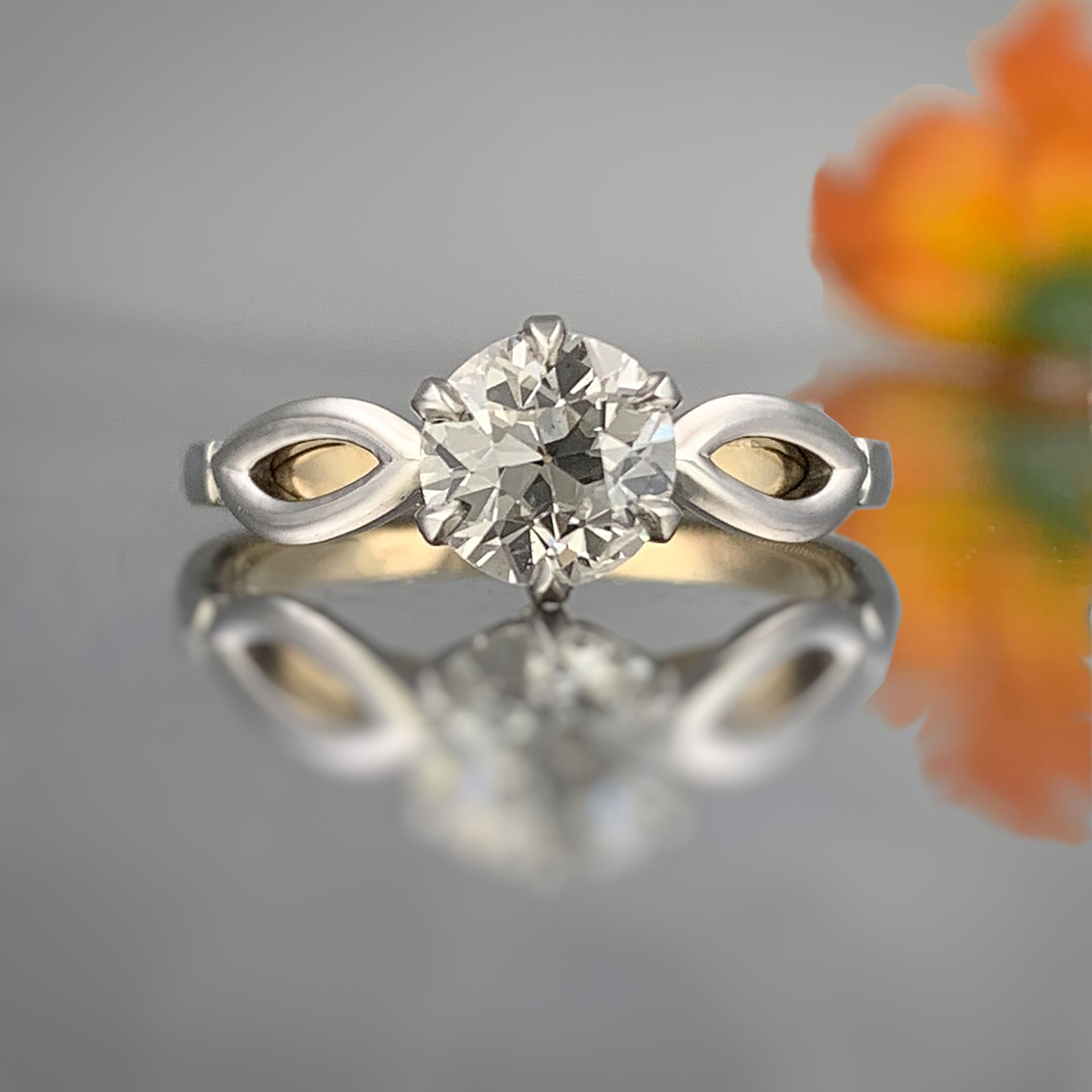 A diamond ring is sitting on a table in front of a flower
