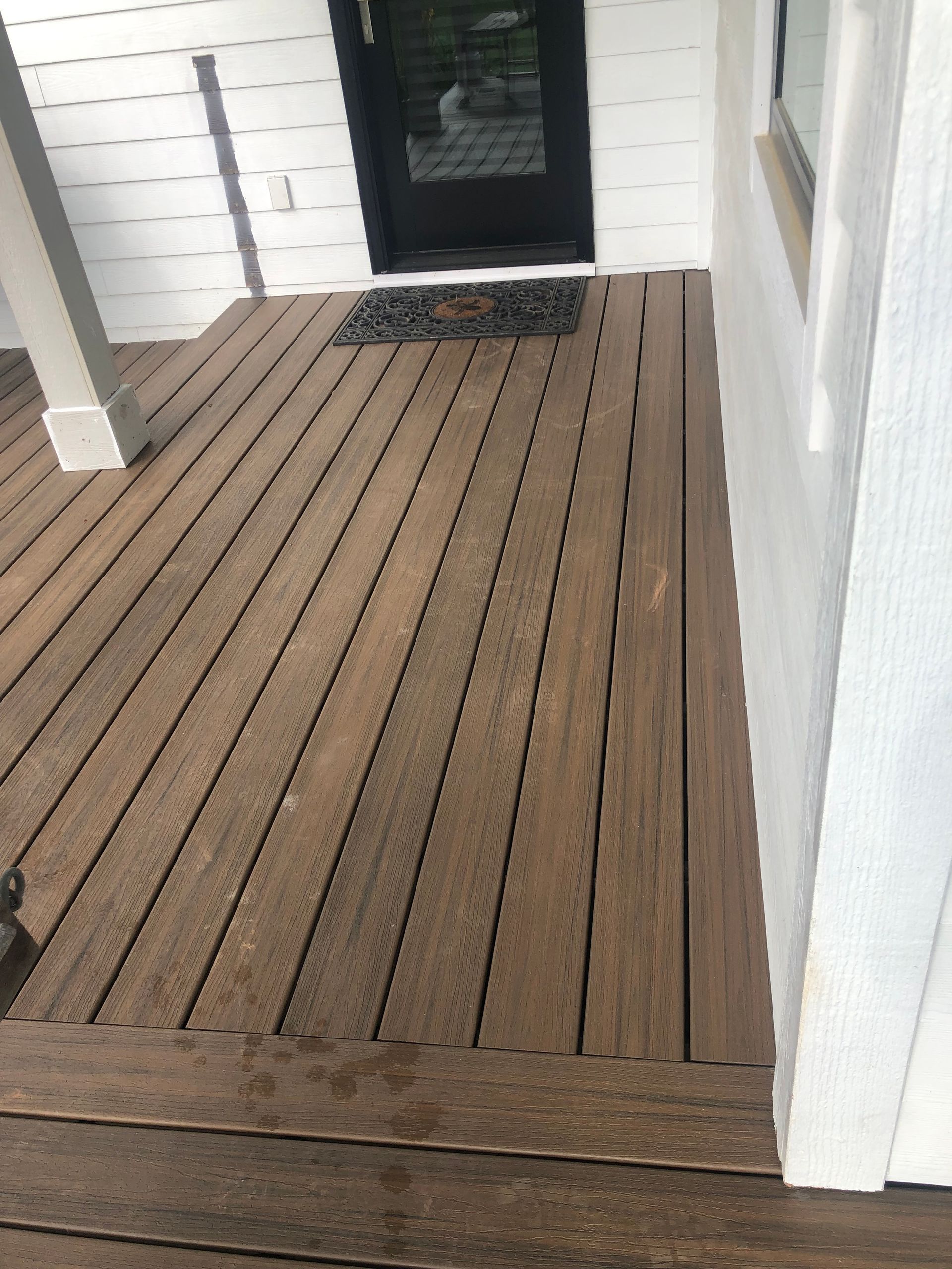 A wooden deck next to a white house with a black door.
