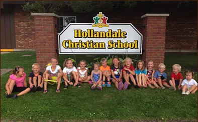 A group of children sit in front of a hollandale christian school sign