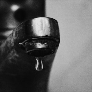 A black and white photo of a faucet with a drop of water coming out of it