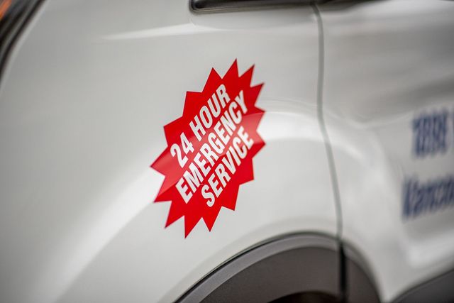 Red 24-hour emergency service decal on a white vehicle door