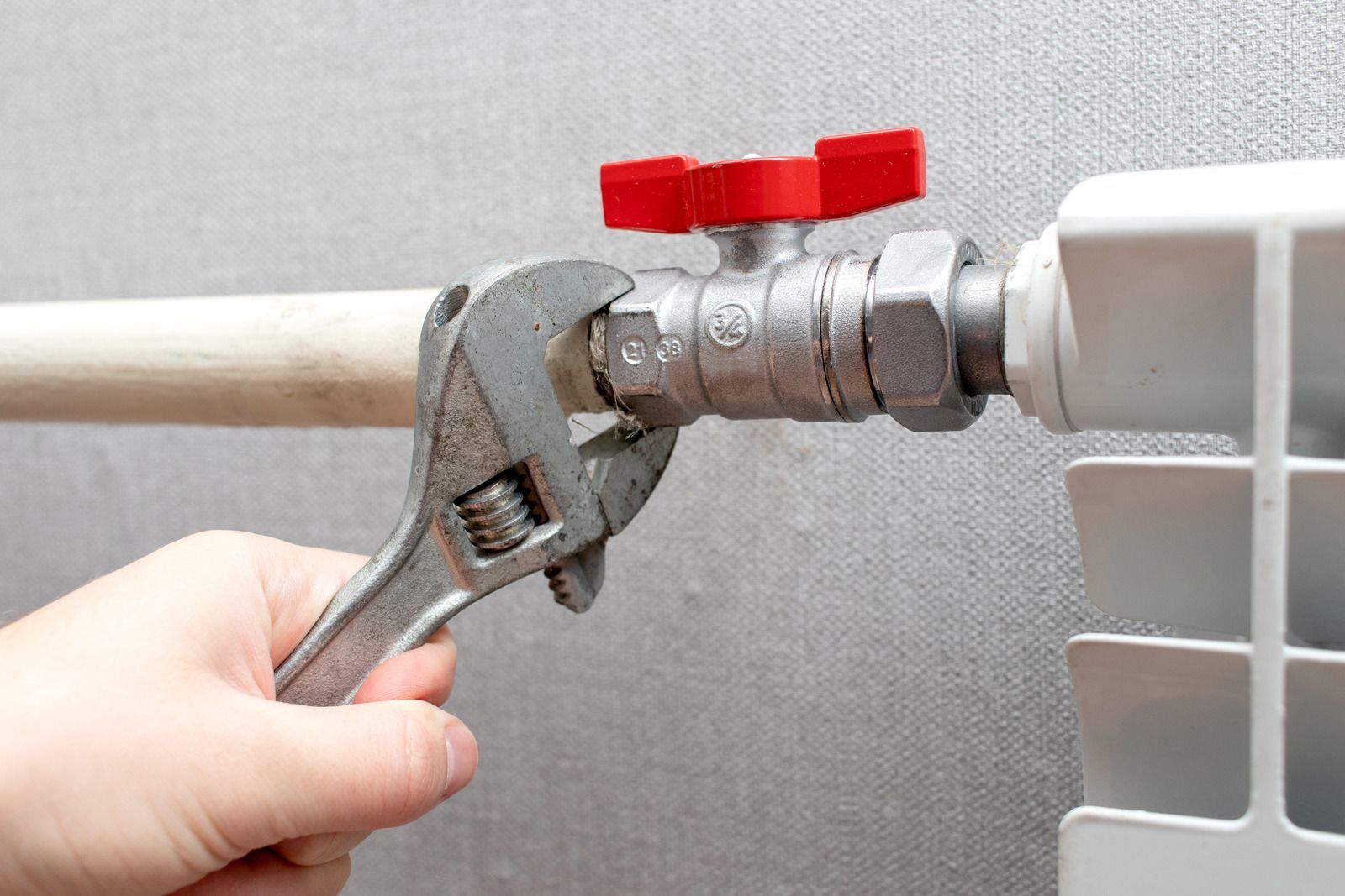 A person is fixing a radiator with a wrench.