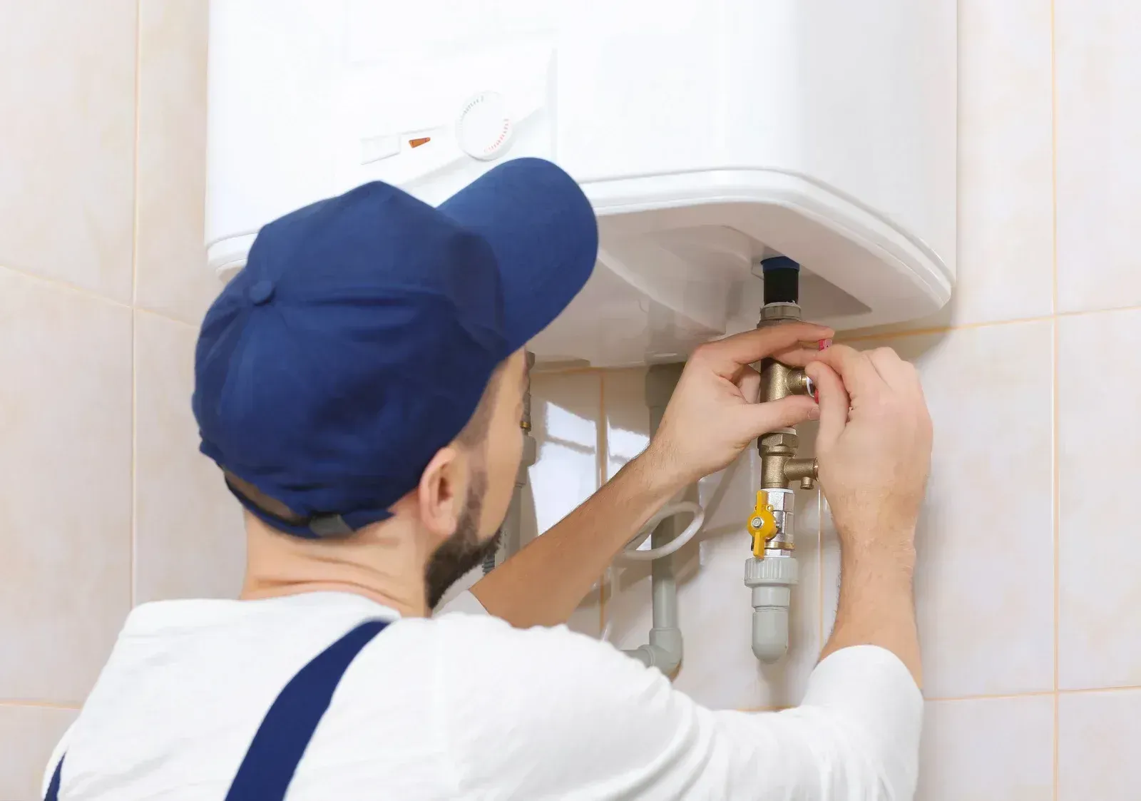 A man is fixing a water heater in a bathroom.