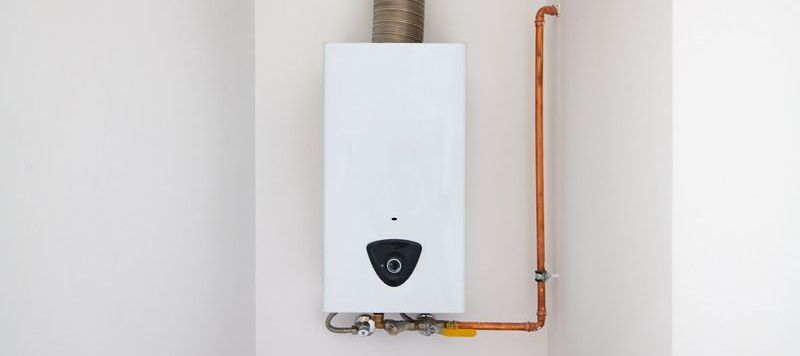 A white water heater is attached to a wall with copper pipes.